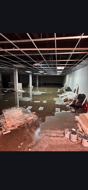 Standing water across the tile floor of a flooded Toronto commercial basement, ceiling grid stripped back